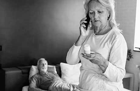 an older woman looking at a pill bottle while calling in a prescription refill